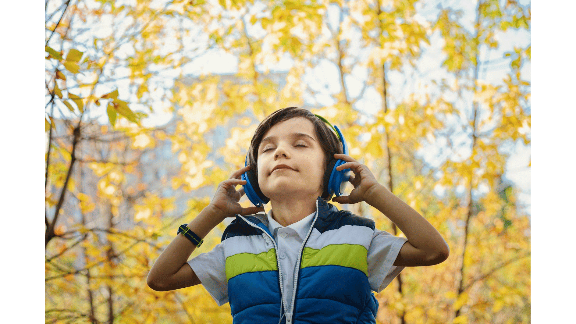 Een jongen met autisme draagt een koptelefoon en geniet met gesloten ogen van de rustige geluiden in een herfstachtig park.